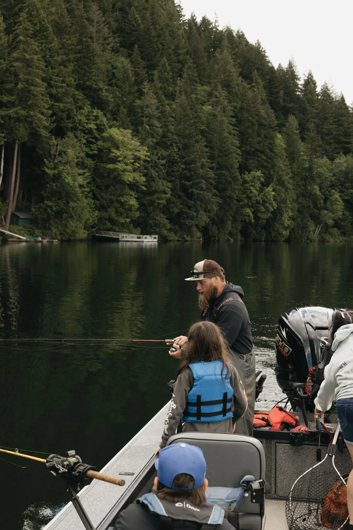 Outdoor instructor helping youth learn to fish from a boat on a Pacific Northwest lake